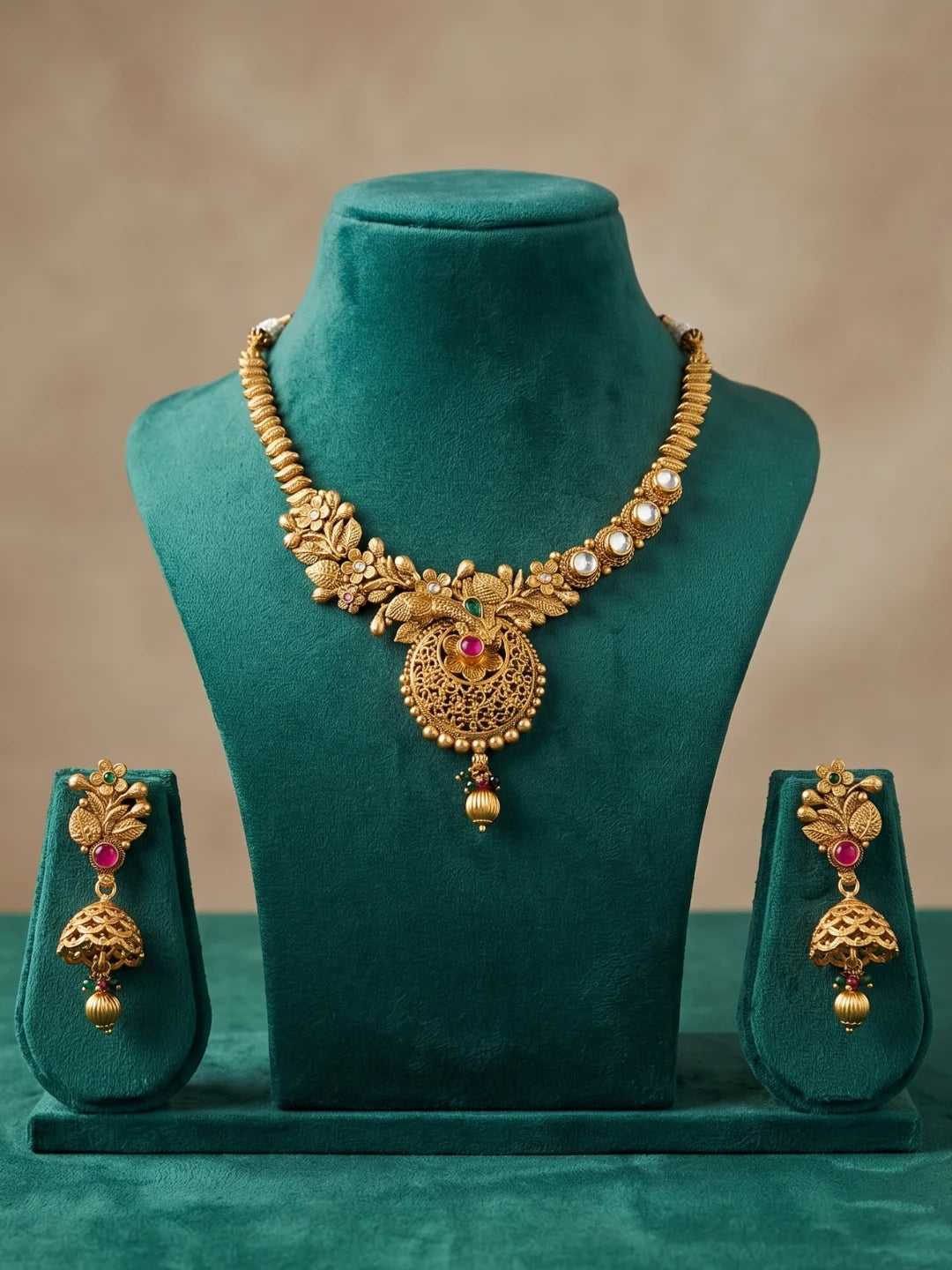 Artificial antique gold necklace with floral motifs, kundan and ruby stones displayed together with matching earrings as a complete jewellery set