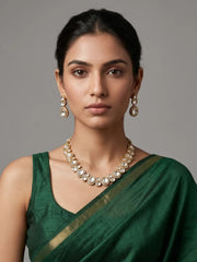 A woman wearing a green sari with a gold border, styled with a gold-toned Kundan necklace and matching drop earrings against a neutral gray background.
