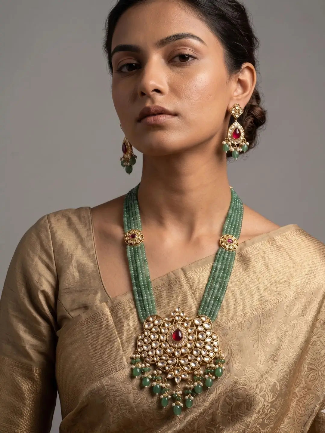 Traditional green jade beaded necklace set with kundan brooches, a large ruby and polki pendant with pearl drops, shown with matching jhumka-style earrings