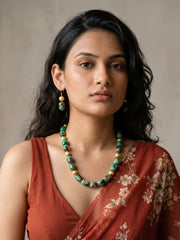 Layered necklace of green shaded chalcedony cylinder beads with gold-plated round spacer beads, laid out in a curve beside a pair of matching drop earrings