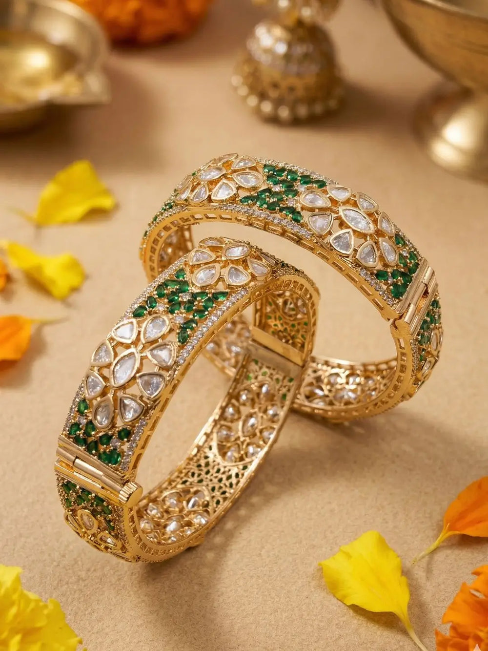 Gold plated ethnic bangles studded with green emerald, CZ and white polki stones on a beige background with decorative elements.