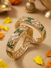 Gold plated ethnic bangles studded with green emerald, CZ and white polki stones on a beige background with decorative elements.