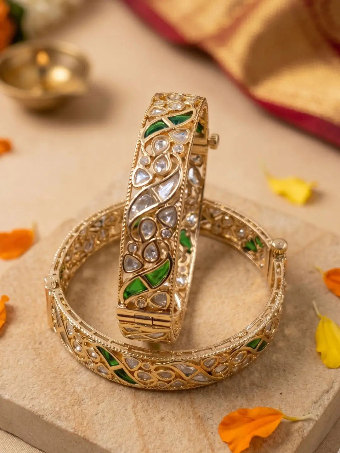 Polki Kundan and green stones studded bangles on a textured surface with orange leaves.