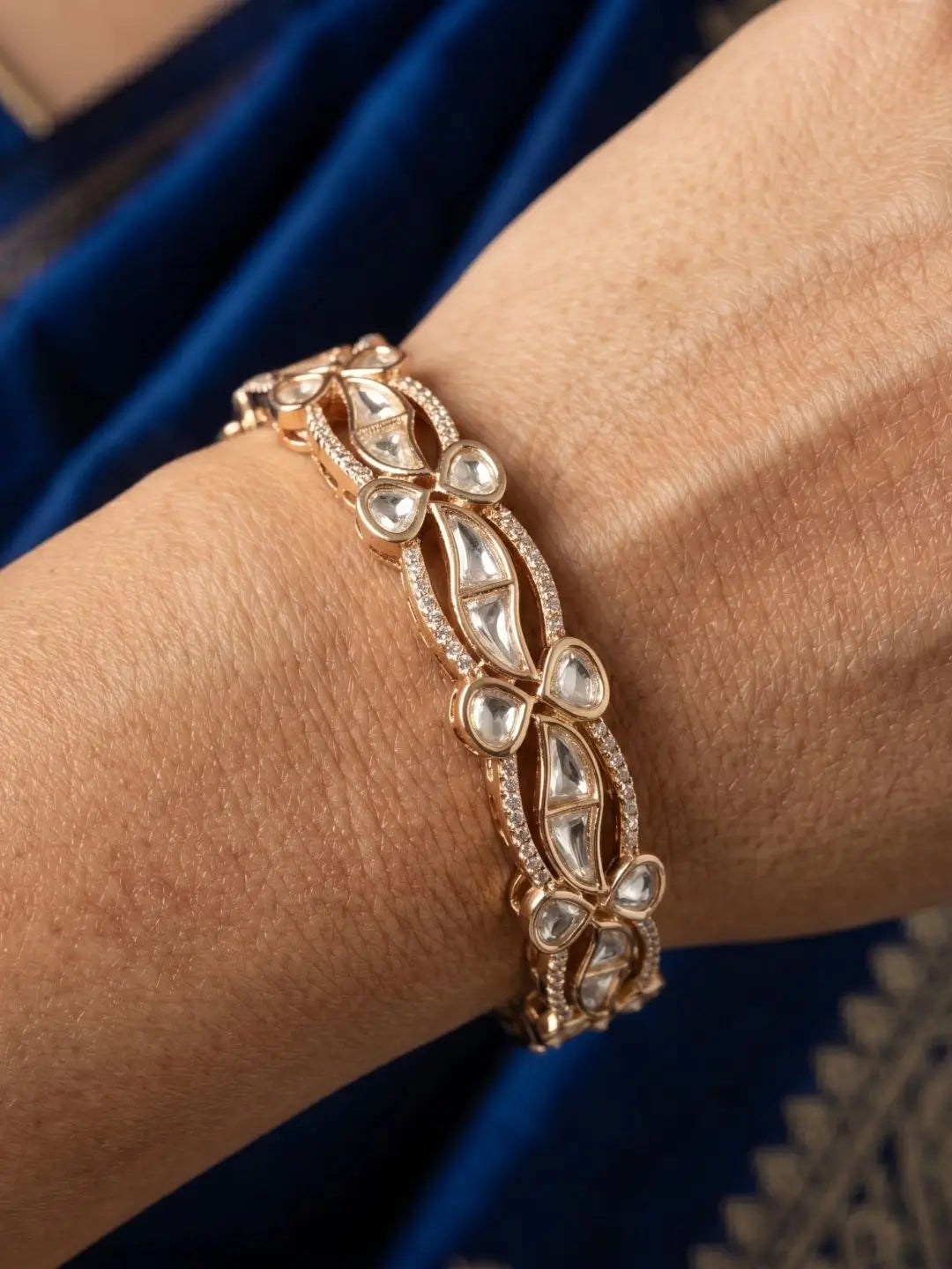 gold plated kundan polki and CZ stones studded bangle on a wrist against a blue fabric background