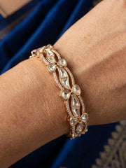 gold plated kundan polki and CZ stones studded bangle on a wrist against a blue fabric background