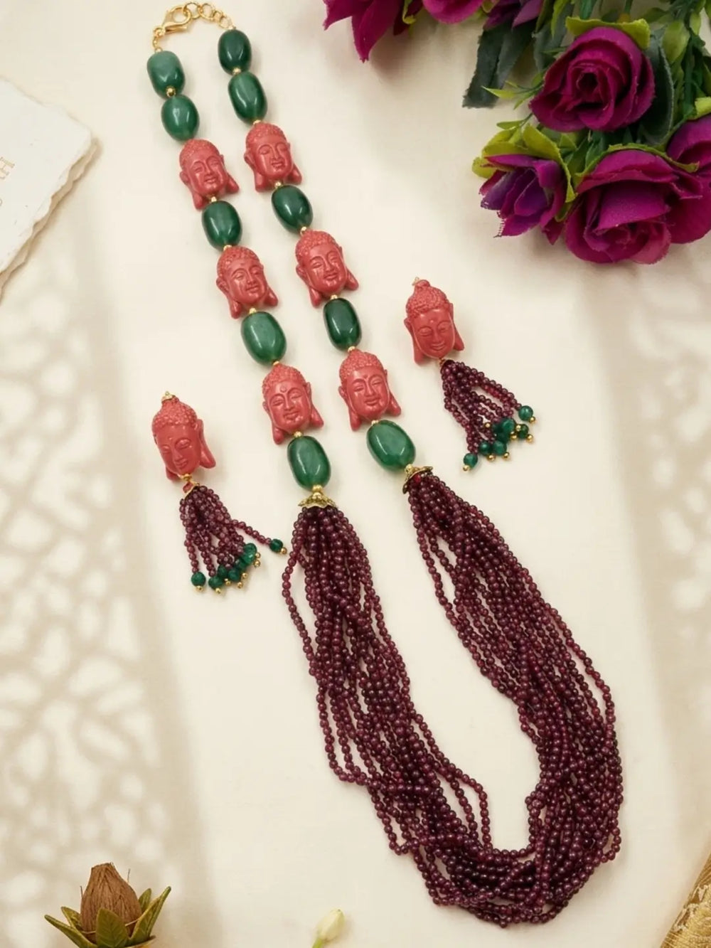 Traditional gemstone bead jewellery set with multiple maroon garnet strands, green jade beads, ceramic Buddha motifs and coordinated earrings.