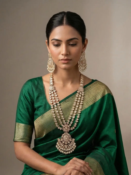 Woman wearing a green saree with a gold border and long layered polki necklace set with a bold pendant jewelry against a neutral background