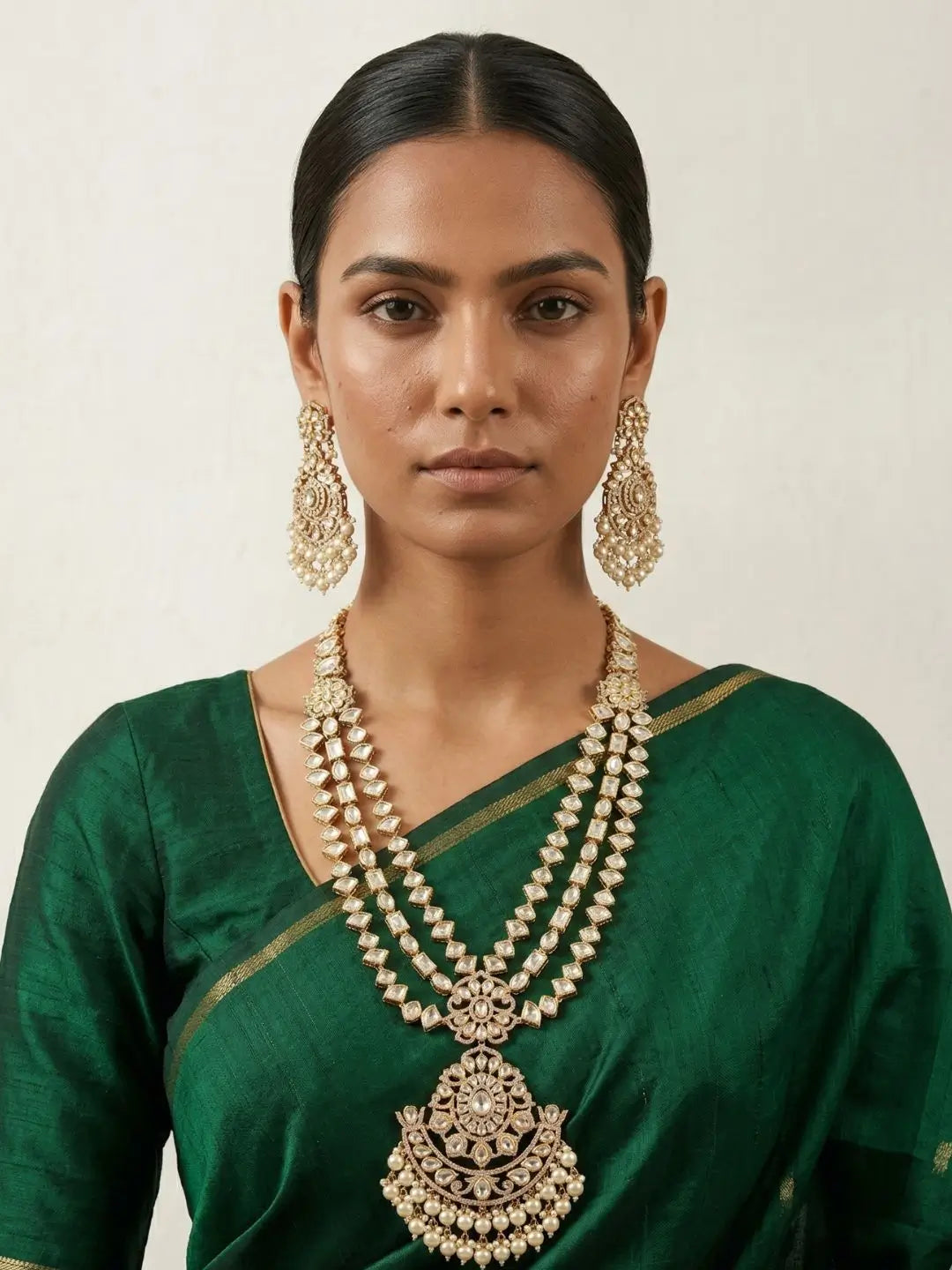 Woman wearing a green saree with gold-plated, long layered polki kundan necklace set on a plain background