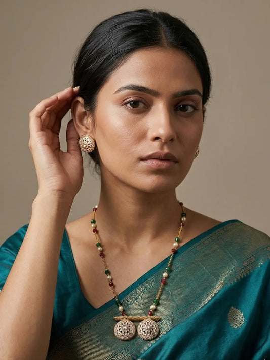 Woman wearing a long multicolour beaded chain necklace with jade beads, faux pearl highlights, a circular Polki Meenakari pendant and matching stud earrings.