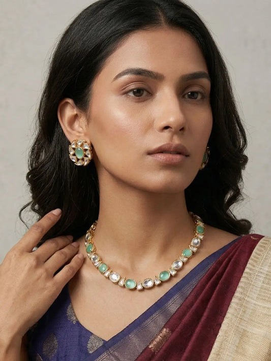 Woman wearing a mint green Kundan necklace featuring alternating Kundan stones and mint coloured cabochons, paired with matching floral stud earrings.