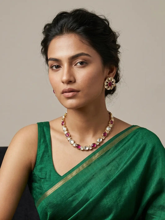 Woman wearing a red Kundan necklace with alternating Kundan stones and vibrant red cabochons, paired with matching floral stud earrings.