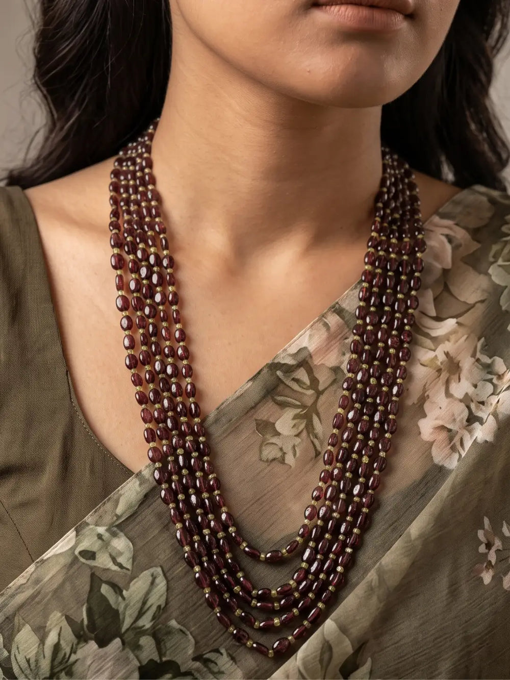 Long multi-strand necklace of polished oval wine-red garnet beads with green peridot spacers and gold-tone connectors, shown as a full layered necklace
