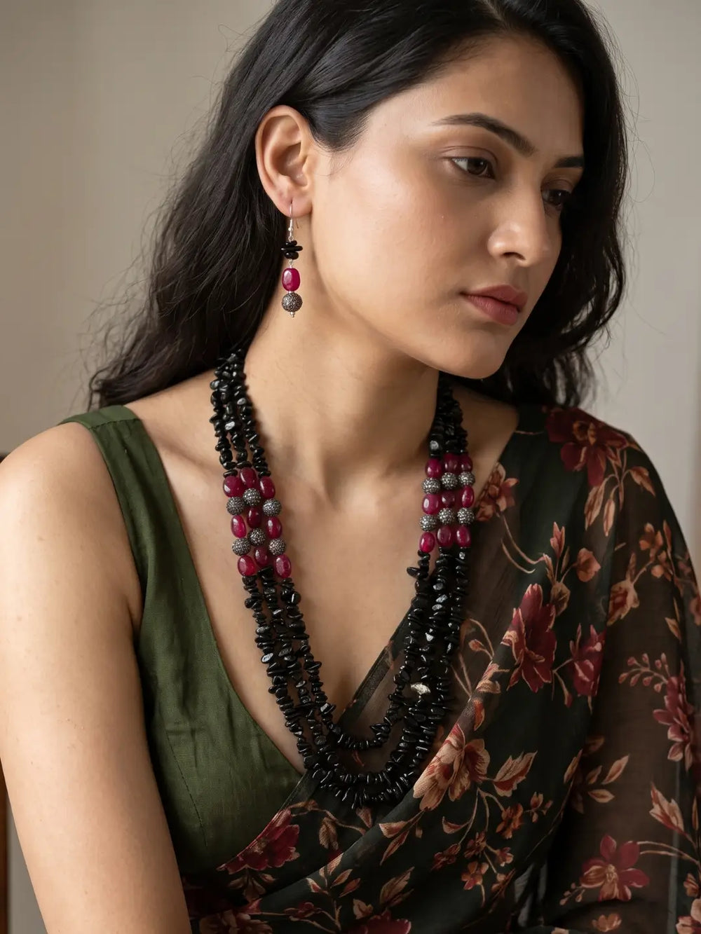 Multi strand necklace of glossy black stone chip beads with red jade and metallic black beads, laid out in a curve beside a pair of drop earrings