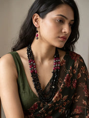 Multi strand necklace of glossy black stone chip beads with red jade and metallic black beads, laid out in a curve beside a pair of drop earrings
