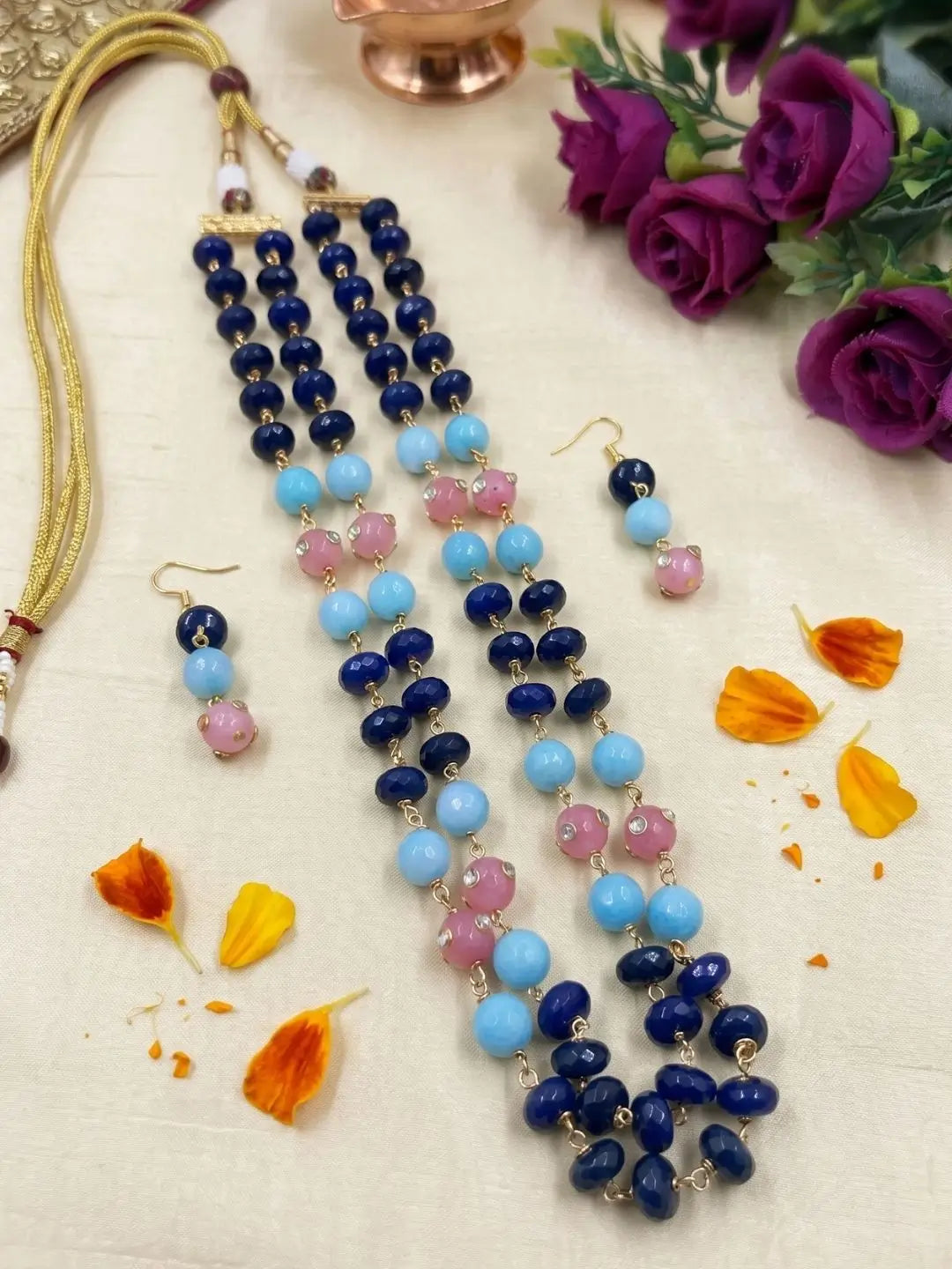 A traditional Indian jewelry set featuring a long beaded necklace and matching drop earrings. The necklace and earrings are made with dark blue jade , light blue, and pink beads, separated by small gold-toned spacer beads.