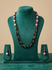 A jewelry set displayed on a teal velvet mannequin bust, featuring a long multi-strand beaded necklace and matching drop earrings with pink round beads and dark metallic spacer details, set against a solid beige background.
