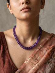 Full view of a long purple amethyst beaded necklace made of a continuous strand of polished natural amethyst beads with gold-plated detailing