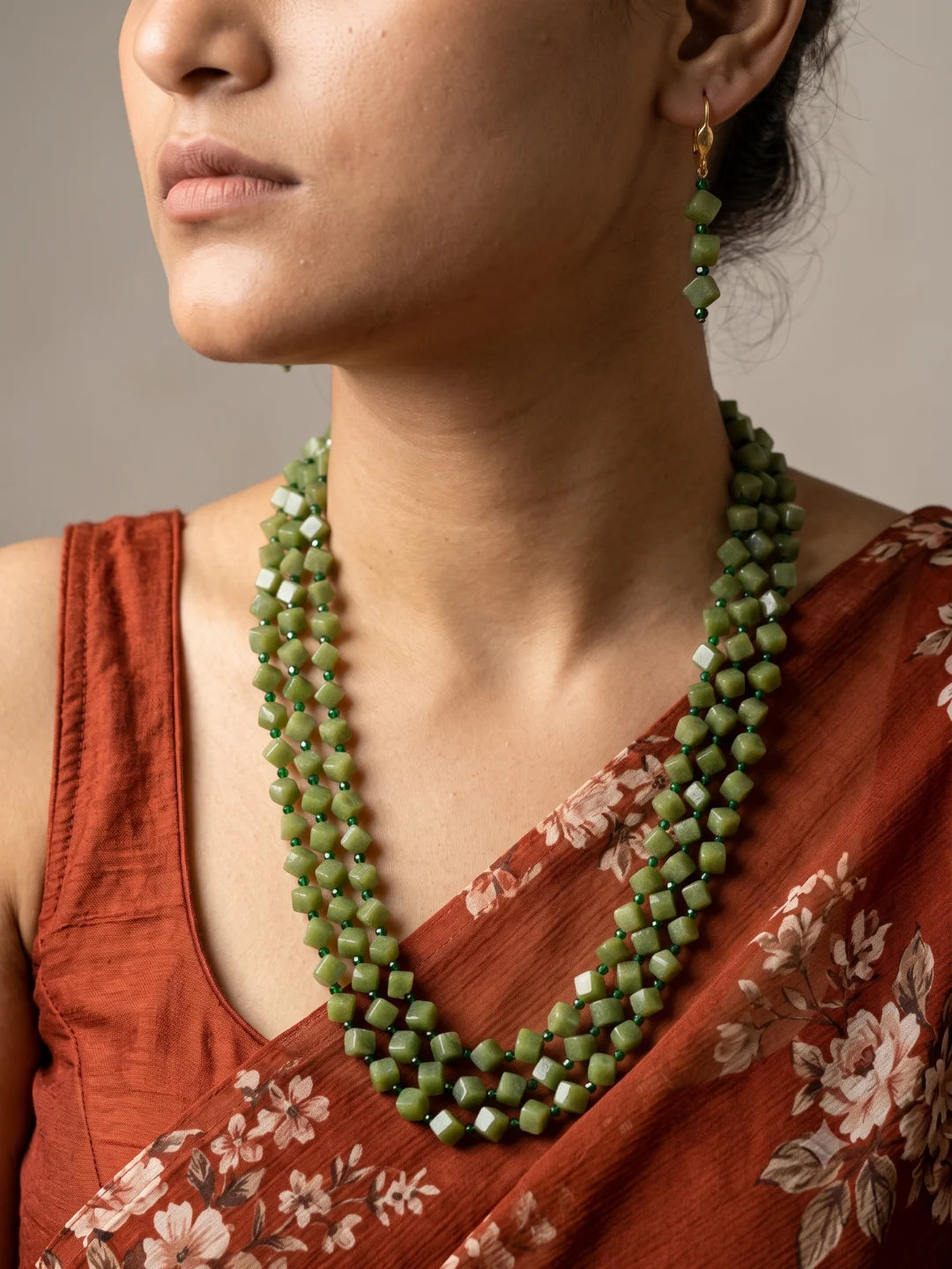 Full view of an olive green layered necklace made of square and cube-shaped beads with dark green spacer beads, shown with matching drop earrings