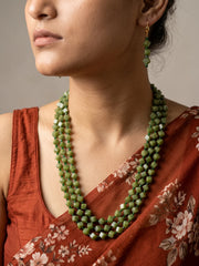 Full view of an olive green layered necklace made of square and cube-shaped beads with dark green spacer beads, shown with matching drop earrings