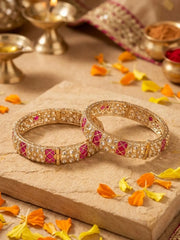 Decorative gold plated bangles with pink and kundan stones on a stone surface with flower petals.h 