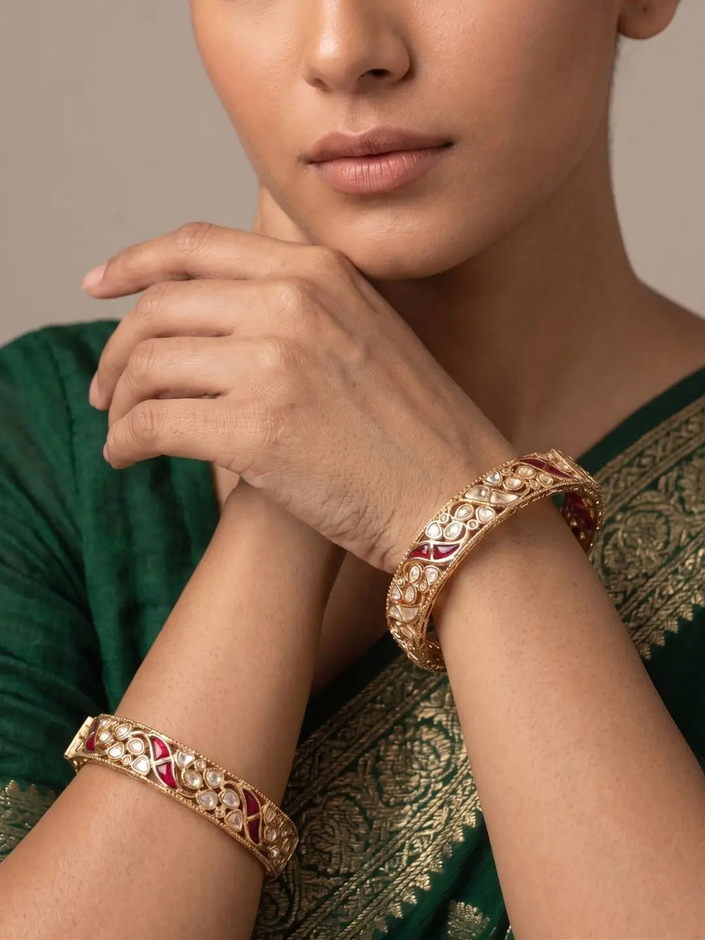 Woman wearing gold-plated ruby and polki-studded bangles on a neutral background