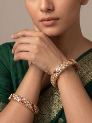 Woman wearing gold-plated ruby and polki-studded bangles on a neutral background