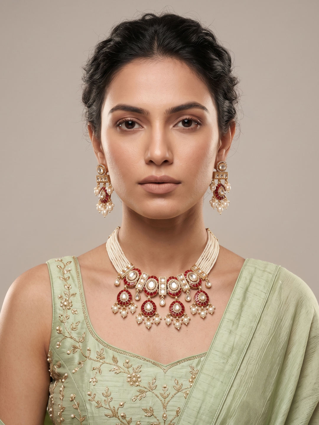 A woman wearing a traditional Indian jewelry choker set featuring a gold-plated necklace and matching earrings with red meenakari and white pearls, paired with a light green embroidered blouse.