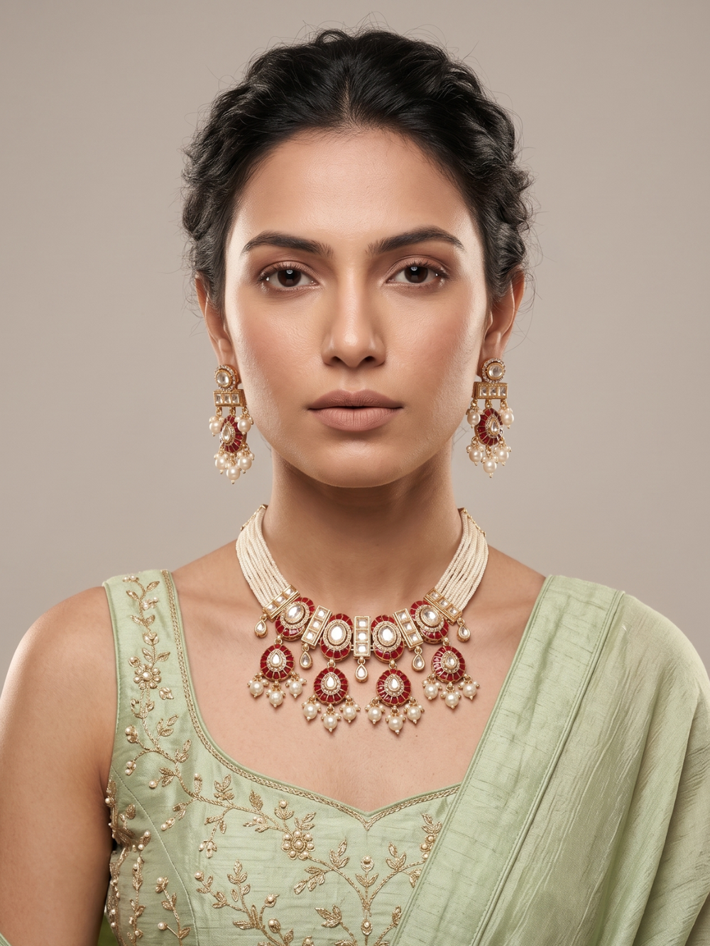 A woman wearing a traditional Indian jewelry choker set featuring a gold-plated necklace and matching earrings with red meenakari and white pearls, paired with a light green embroidered blouse.