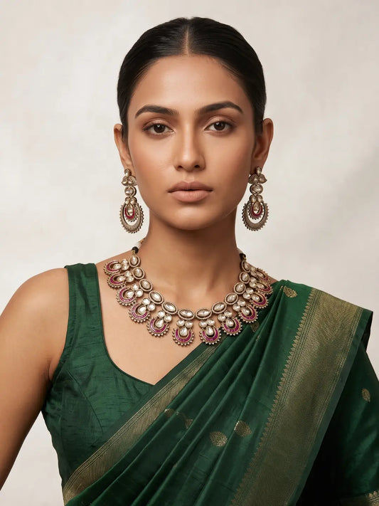 Regal ruby-colored Kundan necklace set featuring layered Polki stonework, teardrop and oval motifs, antique Mehendi plating and coordinated statement earrings.