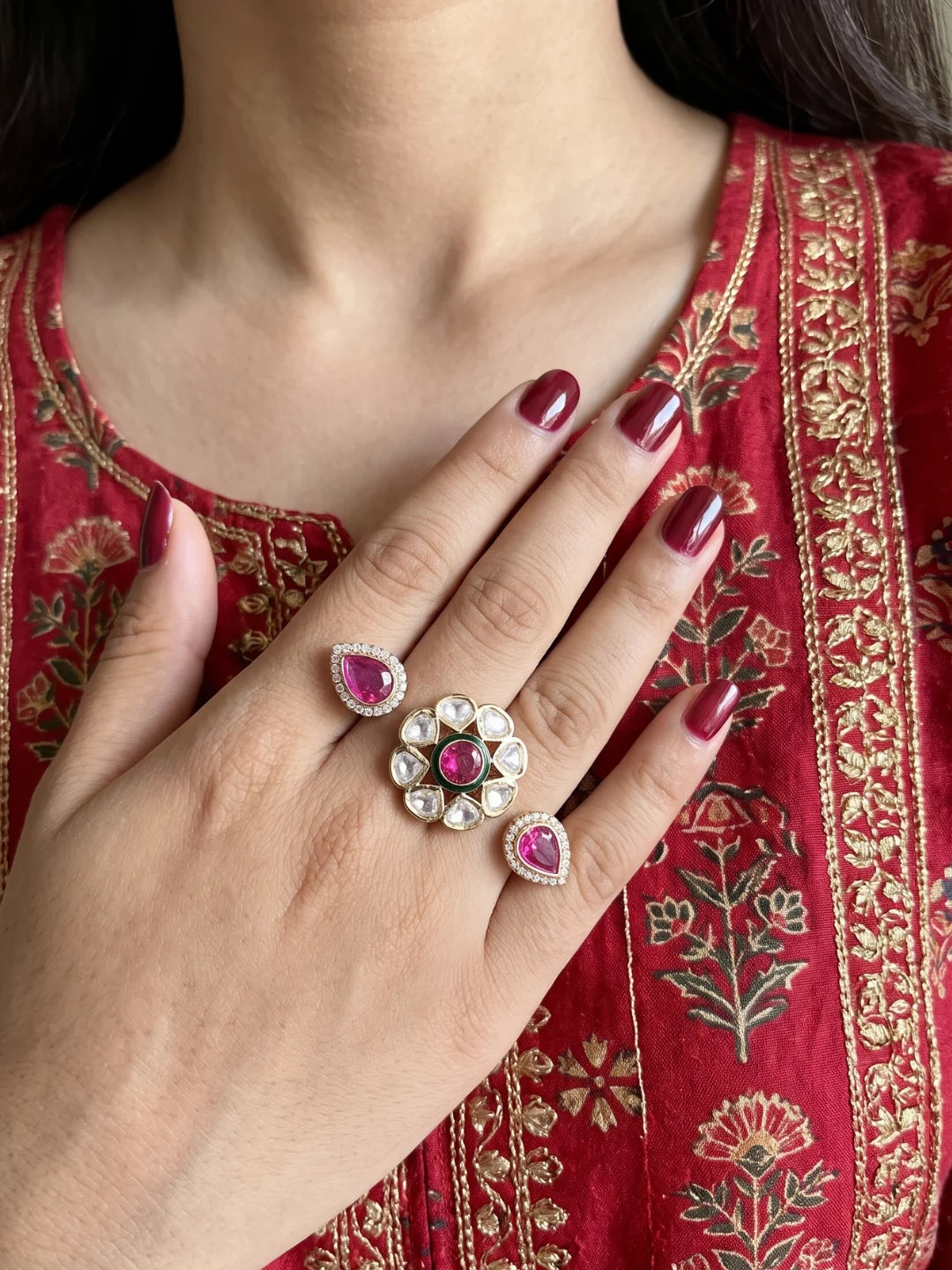 Ruby pink dual-finger Polki ring with a floral centre, matching pear-shaped motifs, CZ stone detailing and a gold-plated finish.