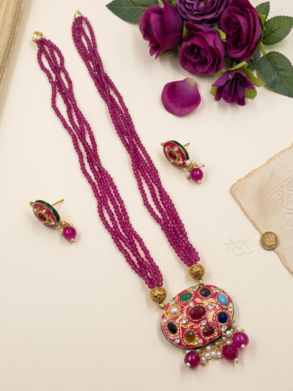 Gold-plated ruby pink necklace set featuring a Navratna Meenakari pendant, layered bead strands and matching stud earrings.