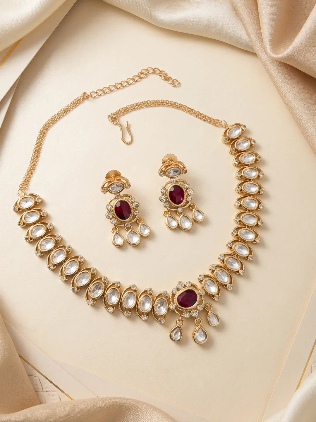 This ruby pink necklace and earring set combines oval Polki motifs, a bold centrepiece, clear CZ stones, and imitation stones in a gold-plated finish.