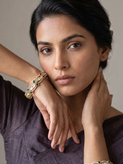 Woman wearing a gold-plated kundan and green stone bangle on her one wrist  with green stones on a neutral background tones