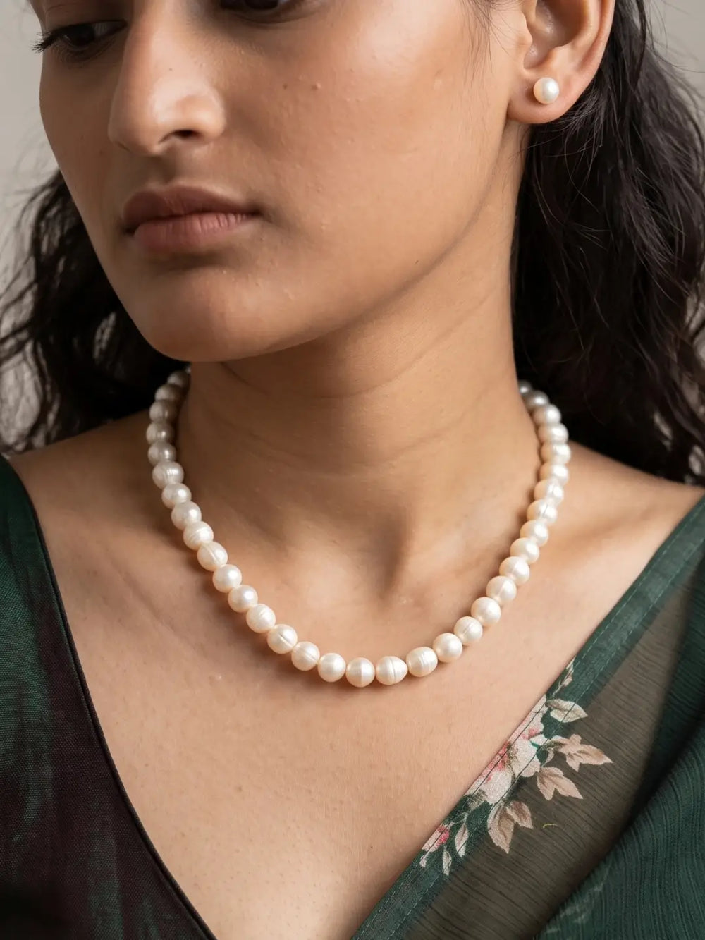 Single strand necklace of round ivory-white freshwater pearl beads laid in a curve beside a pair of matching pearl stud earrings