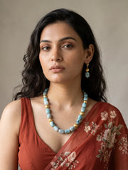 Layered necklace of sky blue shaded chalcedony cylinder beads with gold-plated spacers, laid out in a curve beside a pair of matching drop earrings
