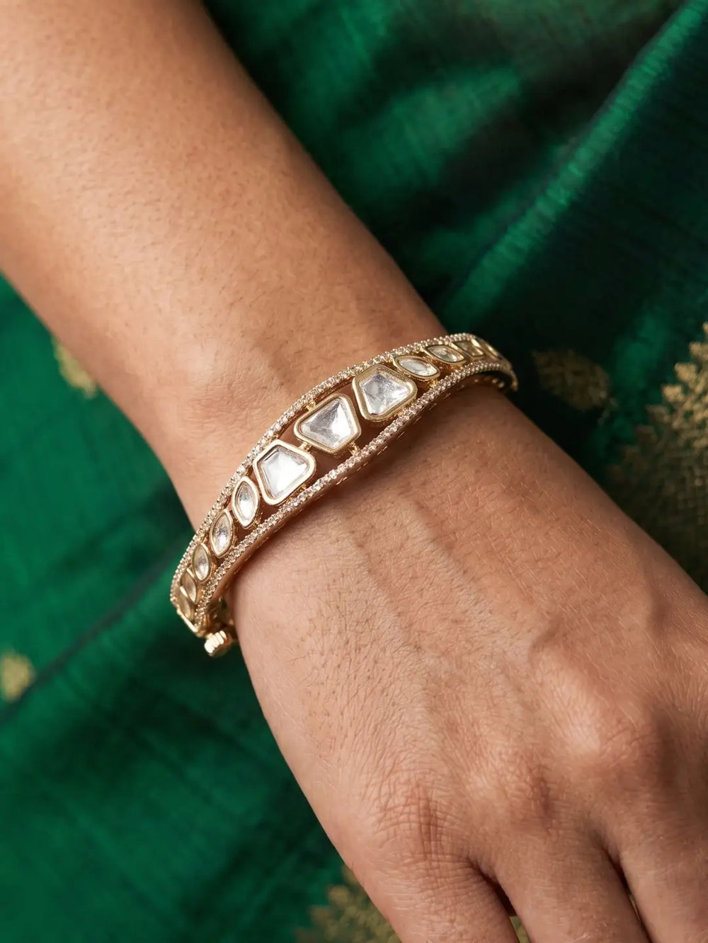 Gold plated kundan bracelet with white stones on a wrist against a green fabric background
