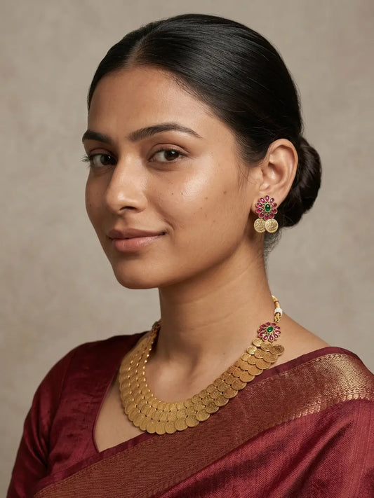 Layered gold-tone temple necklace featuring embossed Lakshmi coins with vibrant red and green floral stone detailing.