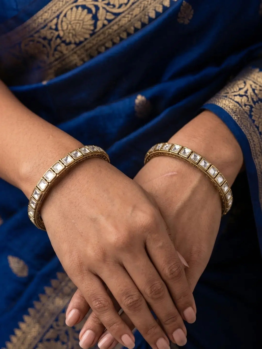Close-up of hands of a women wearing victorian polki square shaped bangles with a blue saree background