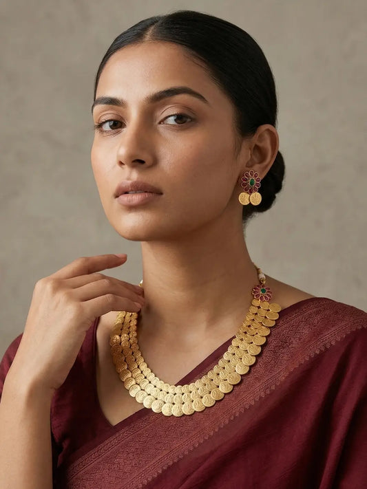 Gold plated temple coin necklace with Lakshmi deity motifs, red and green stone accents and matching earrings for bridal wear.
