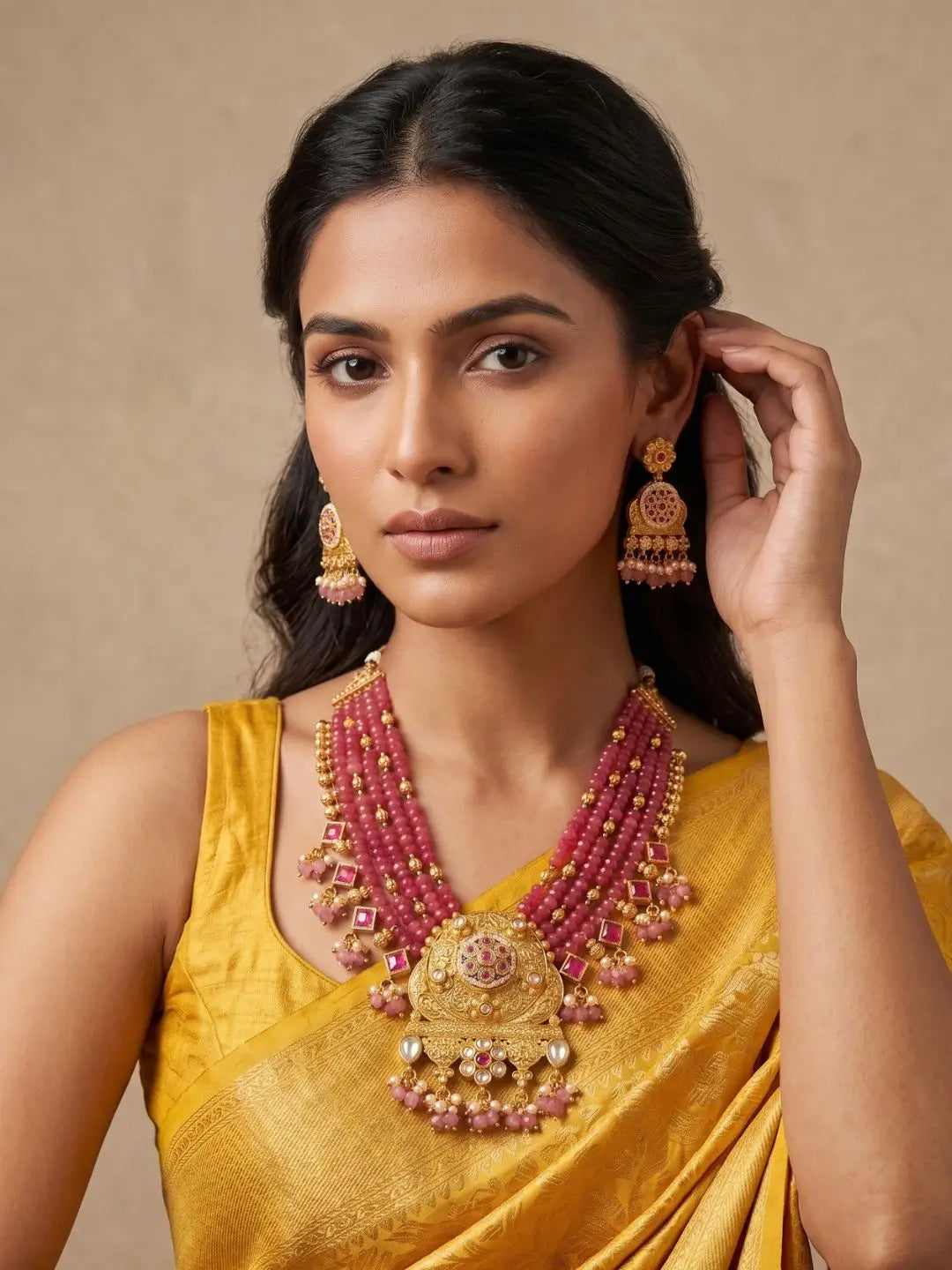 A woman wearing a traditional Indian outfit draped in yellow silk, showcasing multi-strand red antique beaded jewellery with matching dangling earrings.