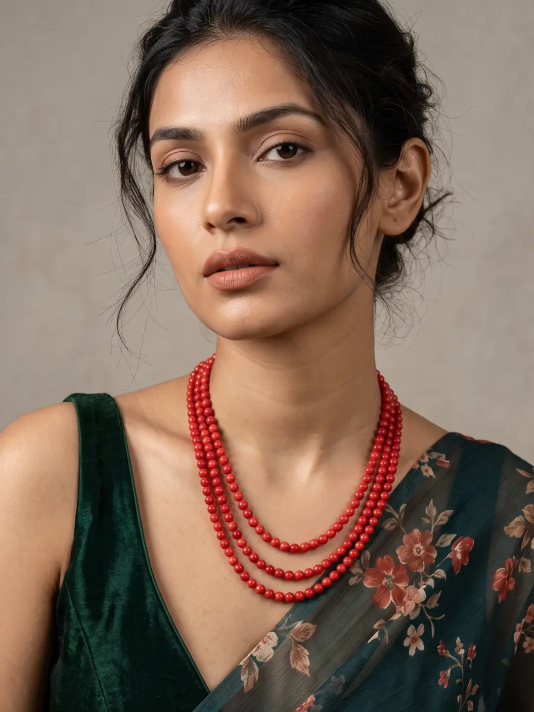 Full view of a three-strand red coral beaded necklace with polished red coral beads arranged in cascading layers and gold-plated detailing