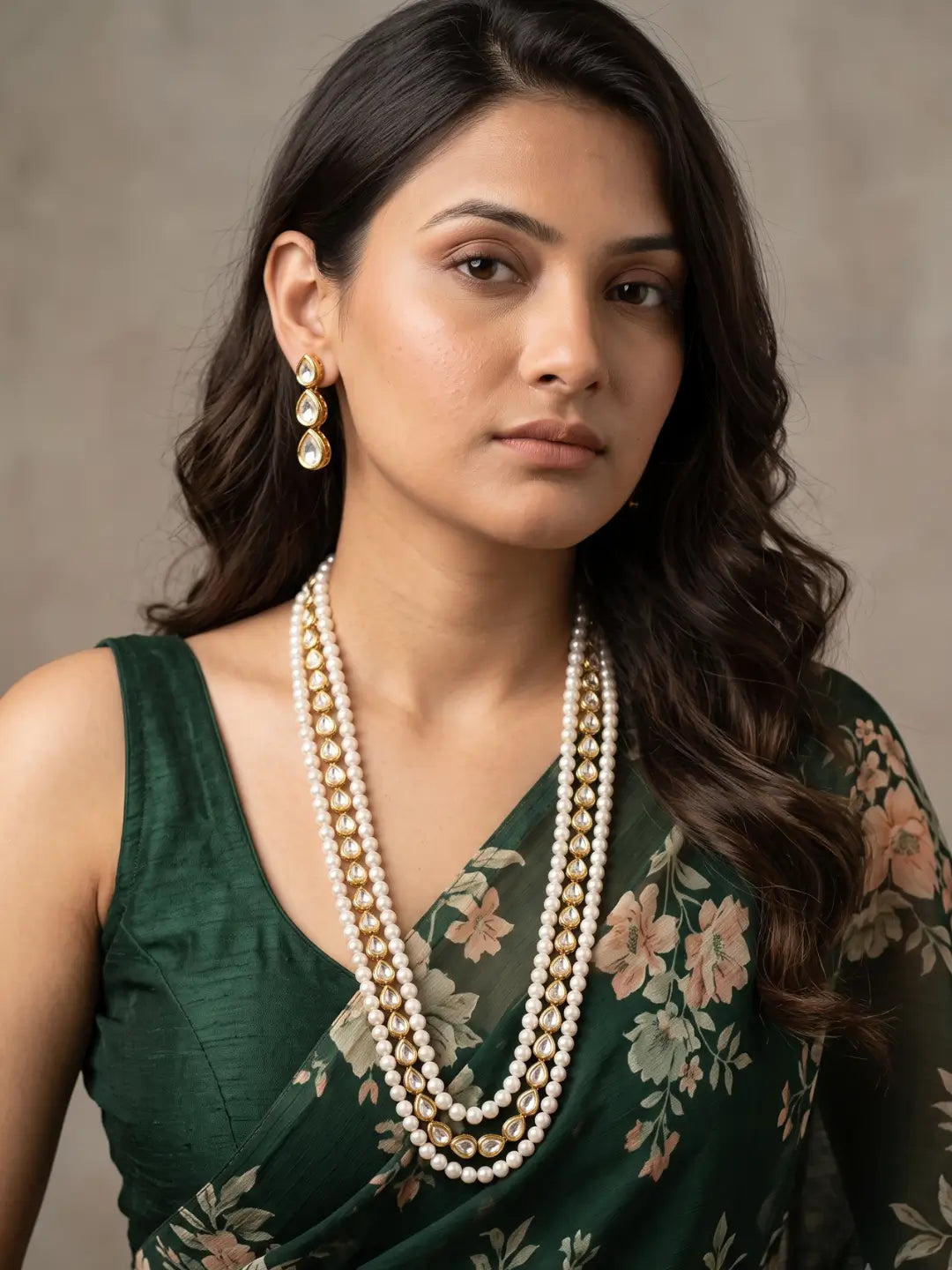 Long necklace of two strands of round white pearls with a teardrop kundan-style centre in a floral pattern, laid out beside a pair of matching earrings