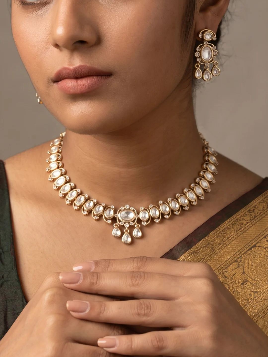 The white Polki choker necklace set features oval floral motifs, clear CZ and imitation stones, a bold centrepiece, and matching dangler earrings.