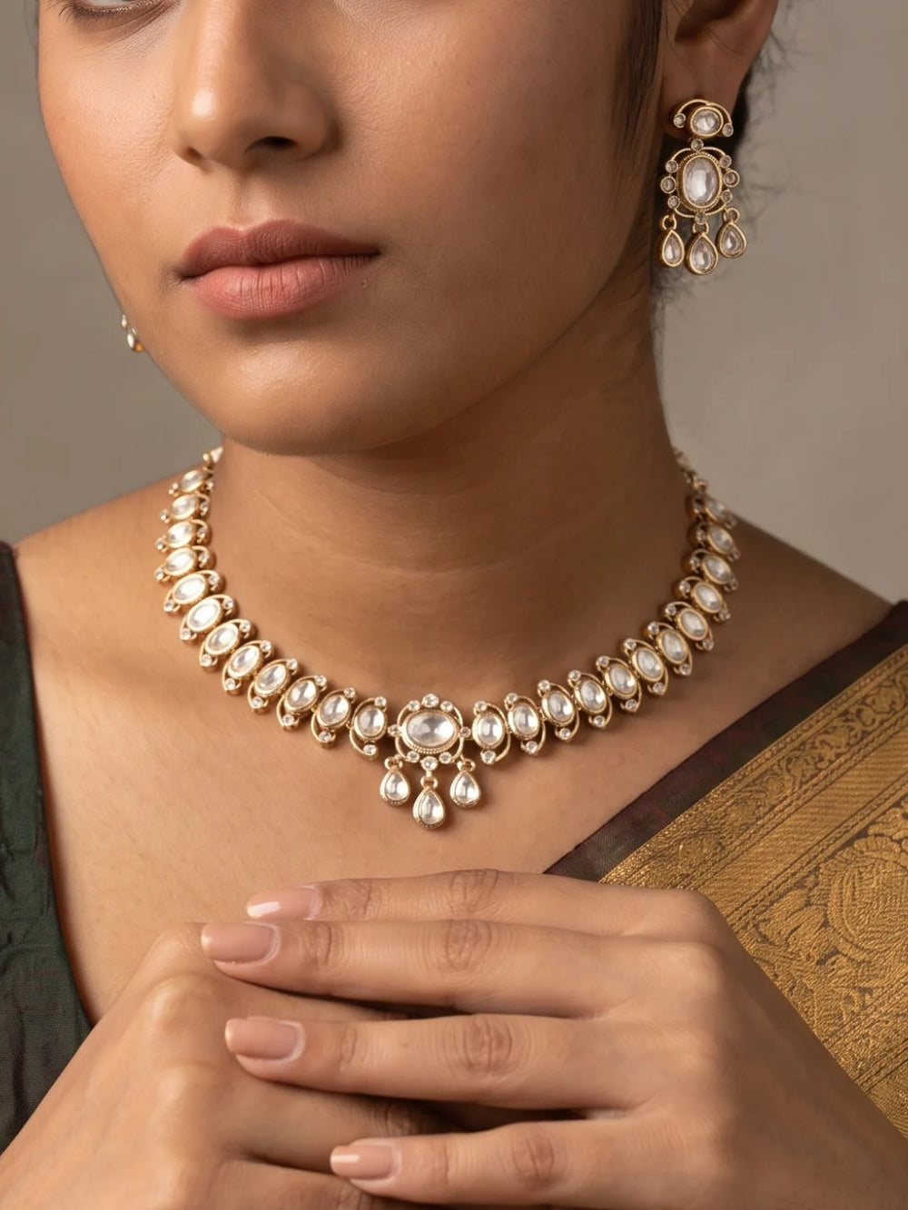 The white Polki choker necklace set features oval floral motifs, clear CZ and imitation stones, a bold centrepiece, and matching dangler earrings.