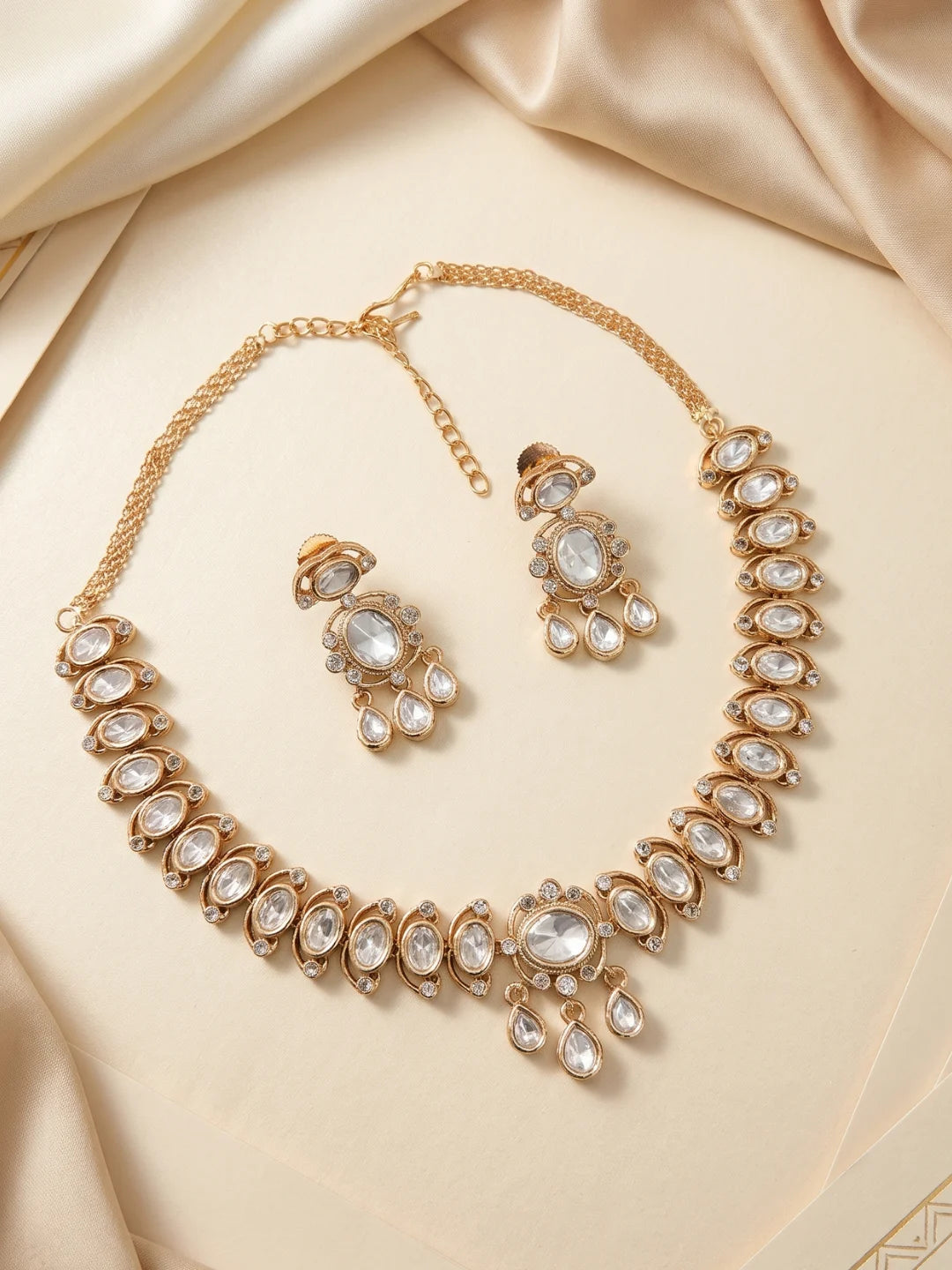 This white necklace and earring set combines oval Polki motifs, a bold centrepiece, clear CZ stones, and imitation stones in a gold-plated finish.