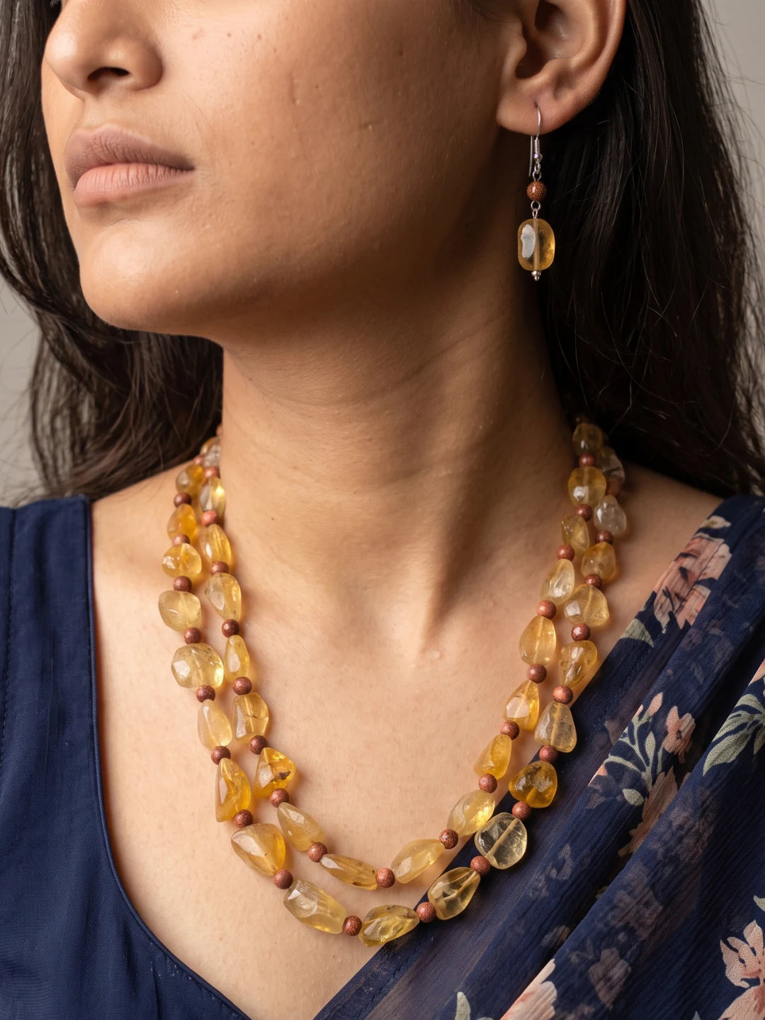 Woman wearing a double strand necklace of faceted yellow citrine and round tiger eye beads with matching drop earrings, shown in a styled view