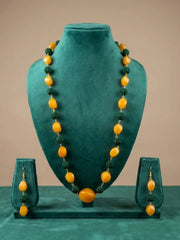 A jewelry set displayed on a teal velvet mannequin bust, featuring a long beaded necklace and matching drop earrings. The beads alternate between smooth, rounded golden-yellow beads and textured dark green beads, with small gold spacers.