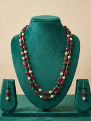A two-strand beaded necklace and matching drop earrings displayed on a dark green velvet jewelry bust. The necklace features alternating strands of deep red faceted beads, cream-colored pearl-like beads, and small green spacer beads, with gold-toned metal findings.