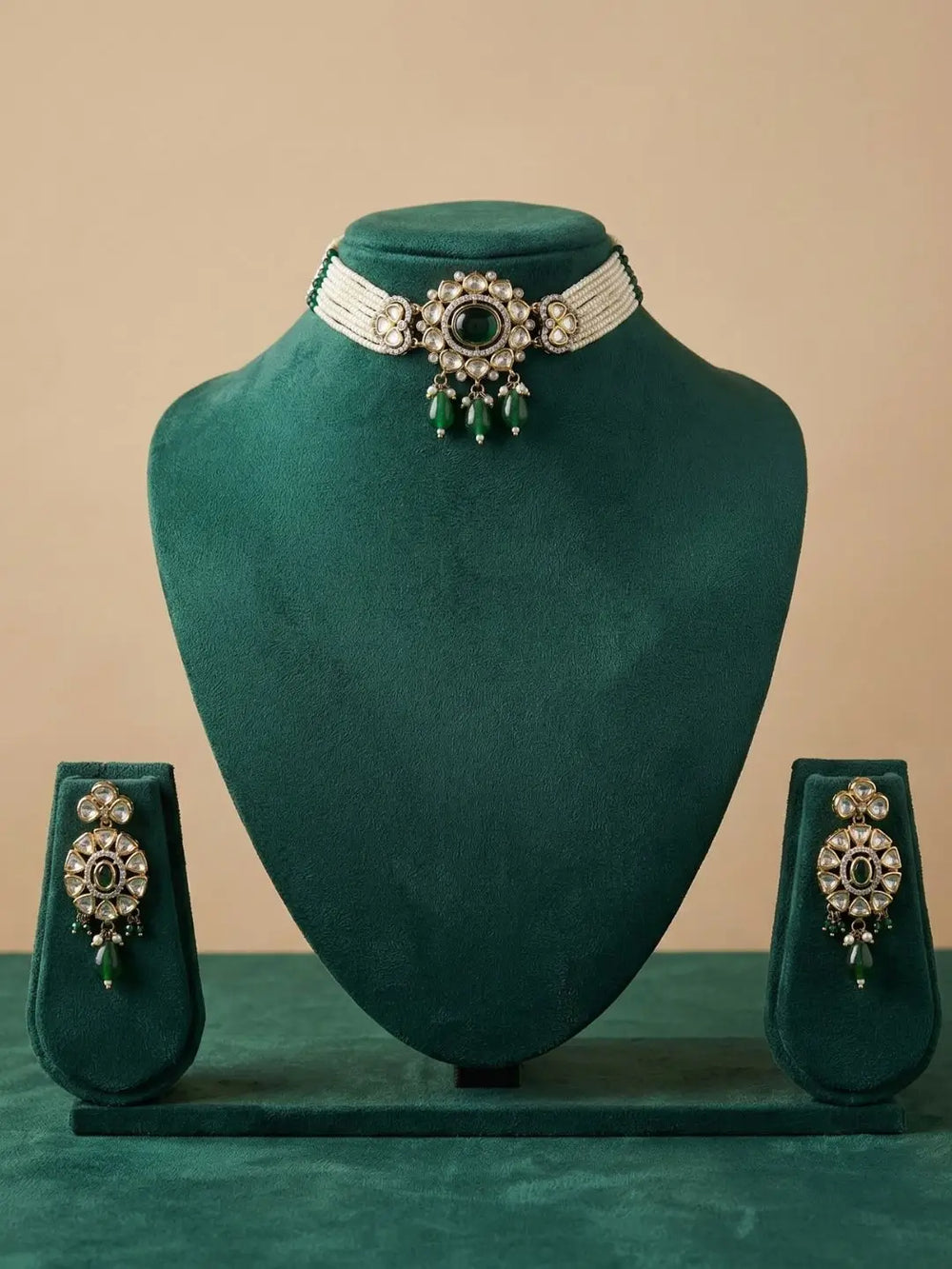 A traditional Indian choker jewelry set displayed on a dark green velvet stand, featuring a silver-toned choker necklace with green bead drops and matching earrings on small display stands.