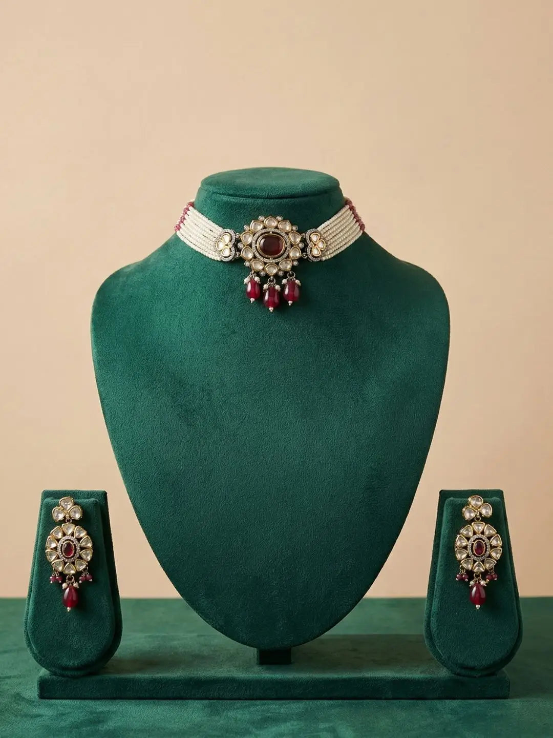Red choker Jewelry set with necklace and earrings on a green velvet stand against a beige background